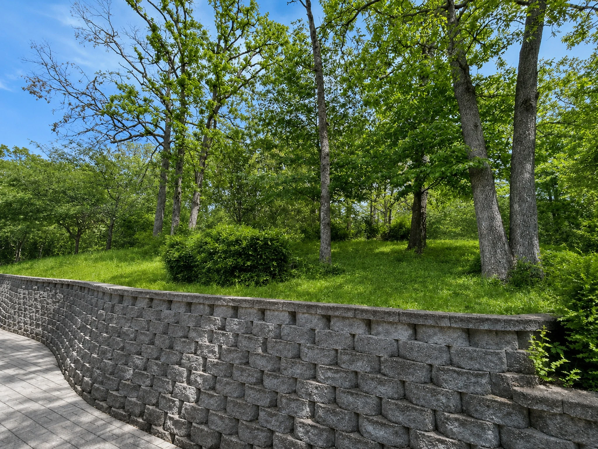 Mature trees and lawn above a stone retaining wall at Morningside Village